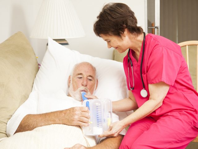 Home health nurse helps a senior patient with his respiratory therapy.