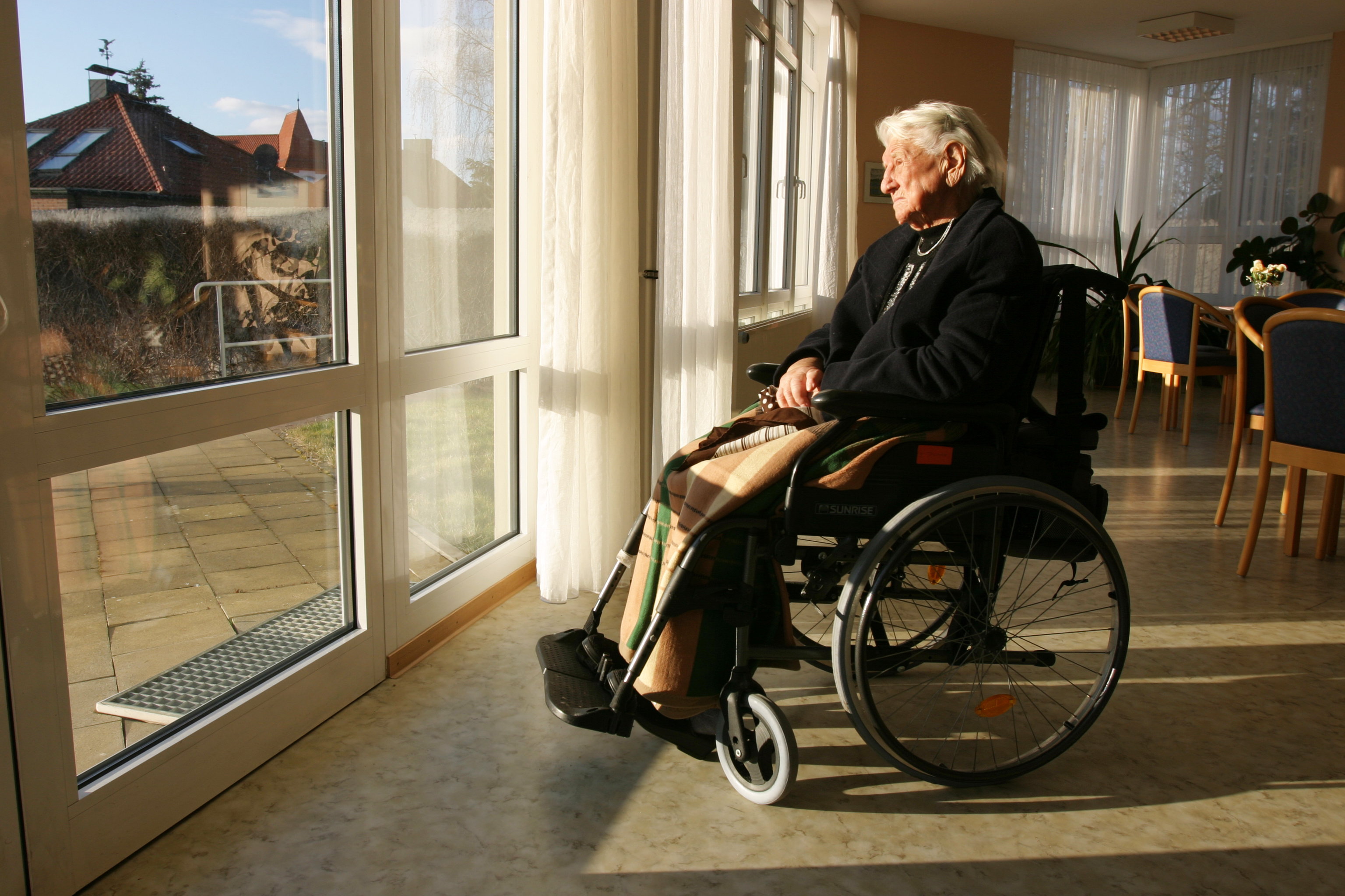 Elderly woman looking out window of lonely nursing home